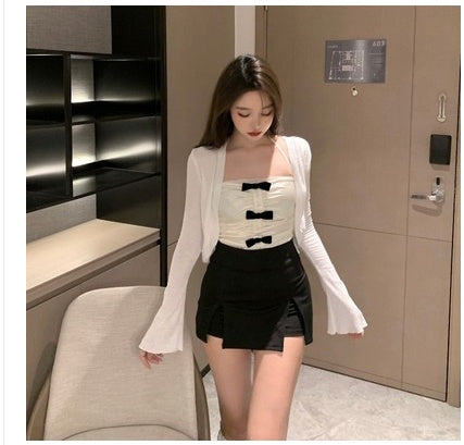 Woman in a stylish outfit with a white cardigan, black top, and skirt in an indoor setting.